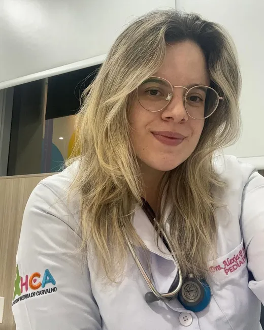 Pediatra Alexia Pinto com jaleco e estetoscópio transmite confiança profissional.